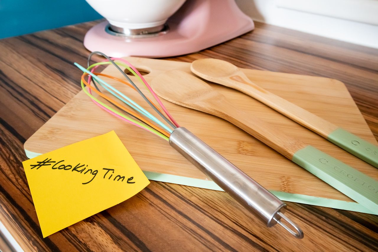 our-experience Colorful kitchen utensils on a bamboo cutting board with a cooking hashtag note, perfect for culinary themes.