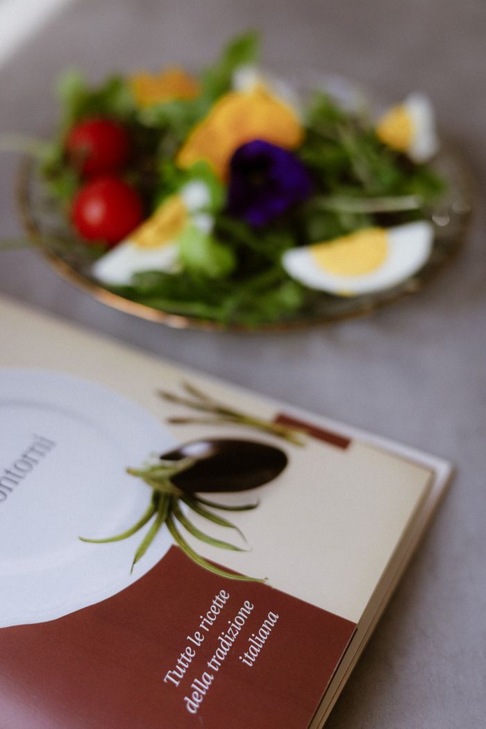 gallery-5 Plate with salad and Italian cookbook on a table, emphasis on healthy eating and culinary inspiration.