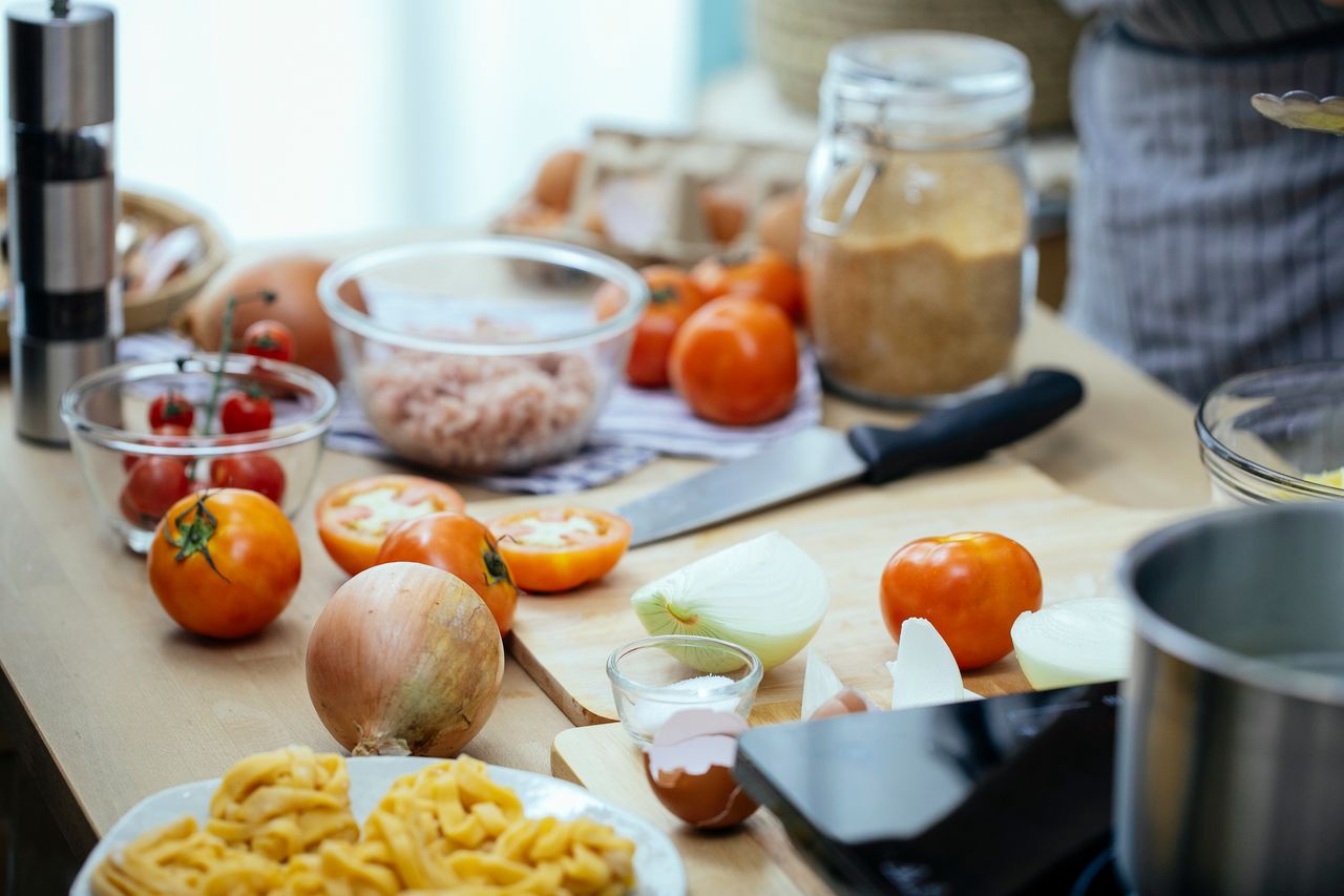 our-services-1 Wooden kitchen countertop with tomatoes and onions and plate of pasta during dinner preparation